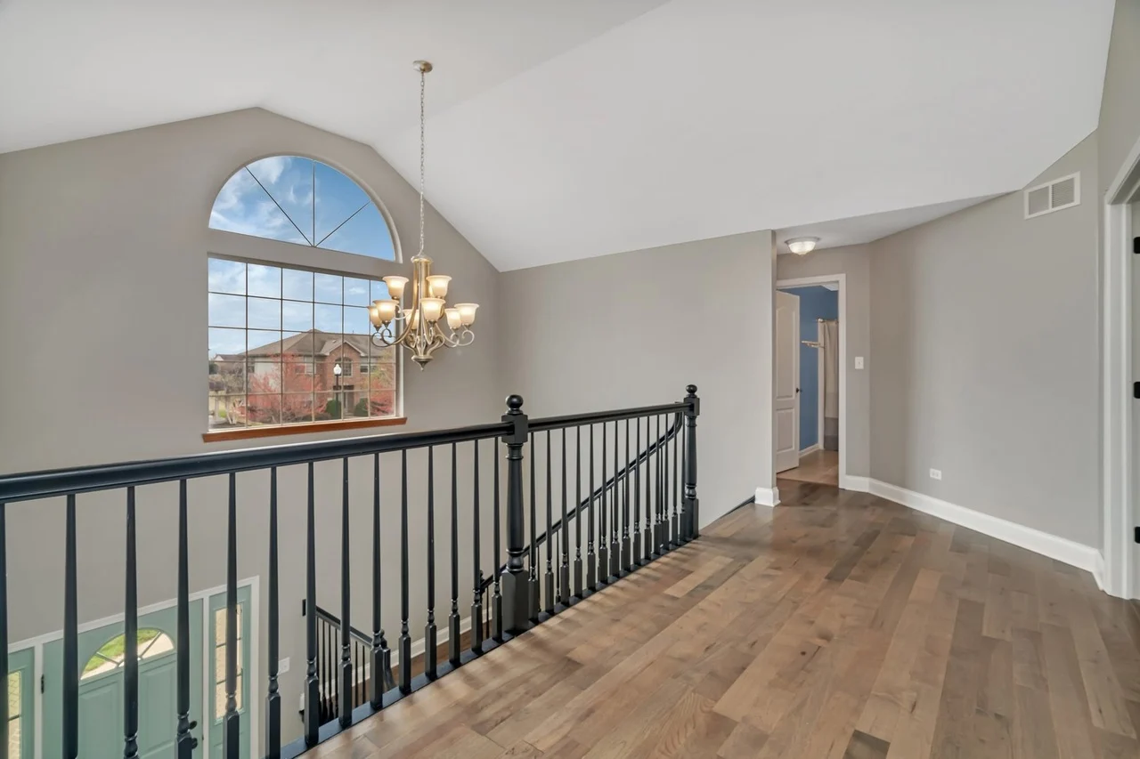 Spacious home interior with staircase, hardwood floors, large windows, and chandelier.
