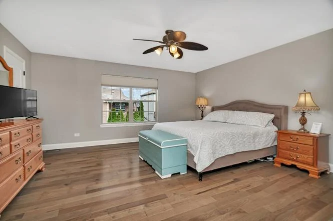Spacious bedroom with large bed, hardwood floors, dresser, ceiling fan, and TV.