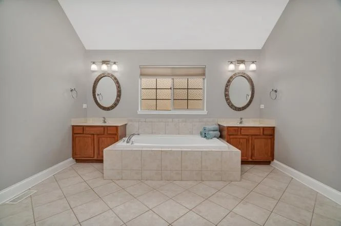 Spacious bathroom with soaking tub, double vanities, round mirrors, and neutral color