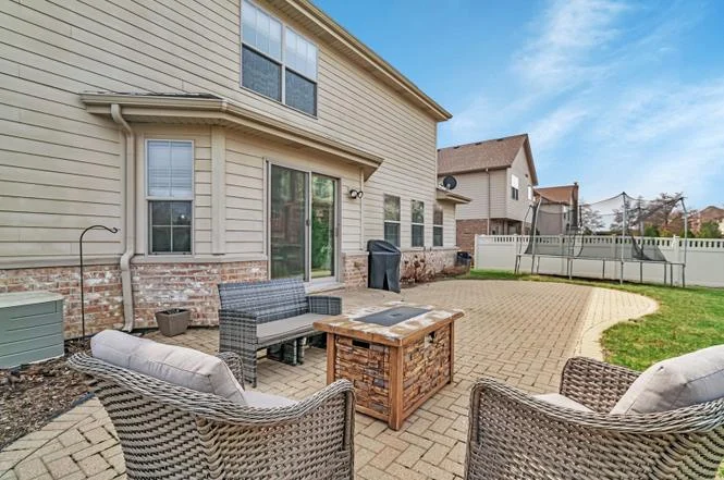 Backyard patio with brick pavers, outdoor seating, fire pit, and house siding.