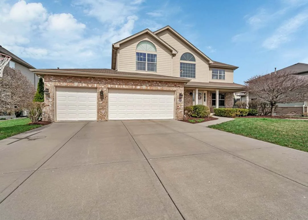 Two-story suburban house with large windows, three-car garage, driveway, and lawn.