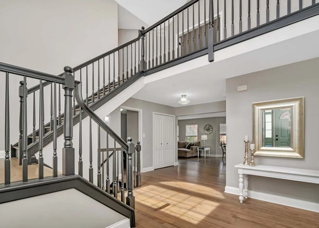 Modern foyer with staircase, dark railings, hardwood floors, and light gray walls.