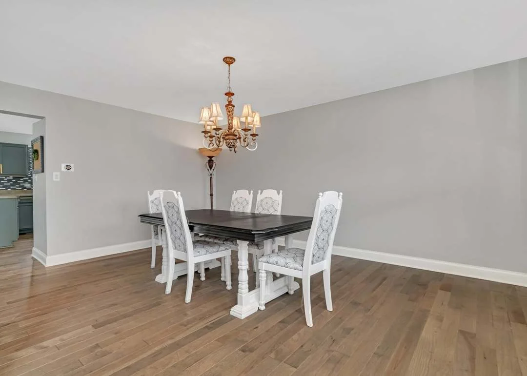 Elegant dining room with dark wood table, white chairs, chandelier, and gray walls.