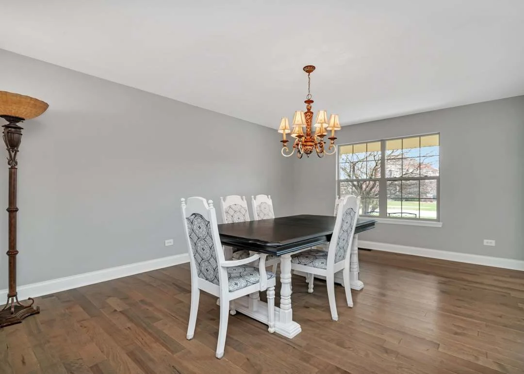 Elegant dining room with dark wood table, white chairs, chandelier, and hardwood floors.