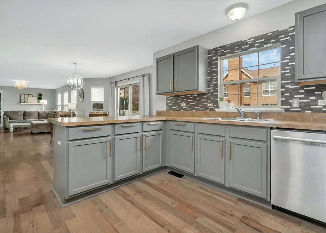 Modern kitchen with gray cabinets, wood countertop, stainless steel appliances, and window view.